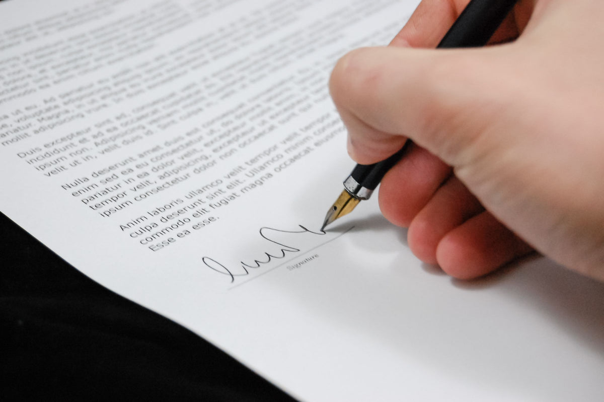 A hand signing a legal document with a fountain pen