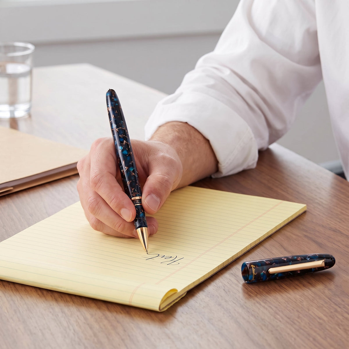 A lawyer in shirtsleeves taking notes on a yellow legal pad with the Esterbrook Estie Rollerball in Nouveau Bleu, the gold rollerball tip on the page and the pen's cap resting on the table beside the pad