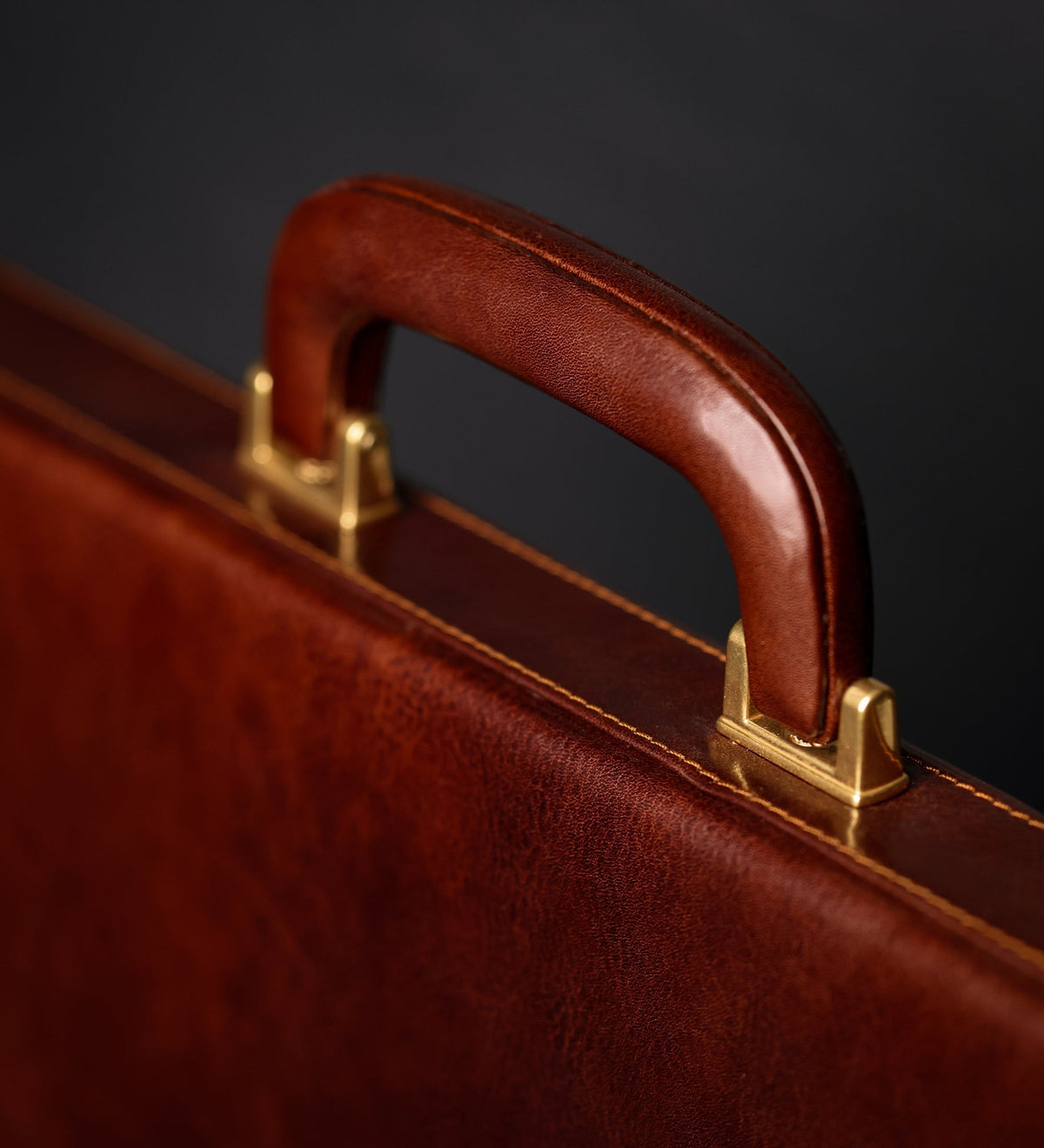 Stitched leather top handle and brass fittings of the Vendetta brown attaché case, close-up