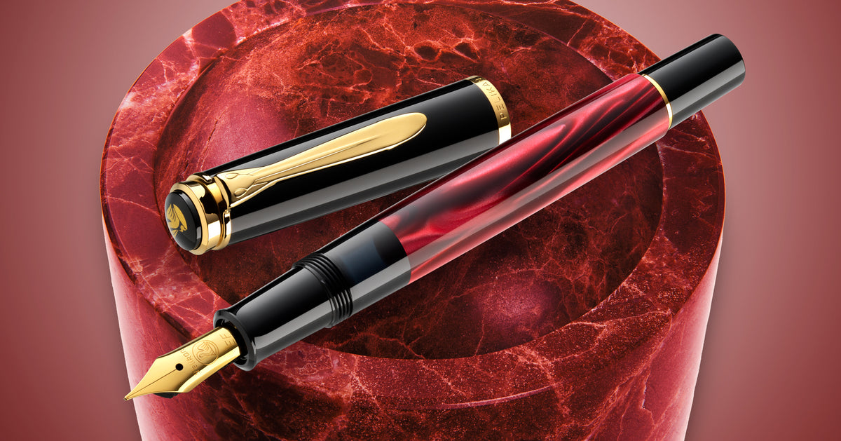 Pelikan M200 fountain pen in red marbled resin with gold trim, uncapped beside its cap on a red marble surface