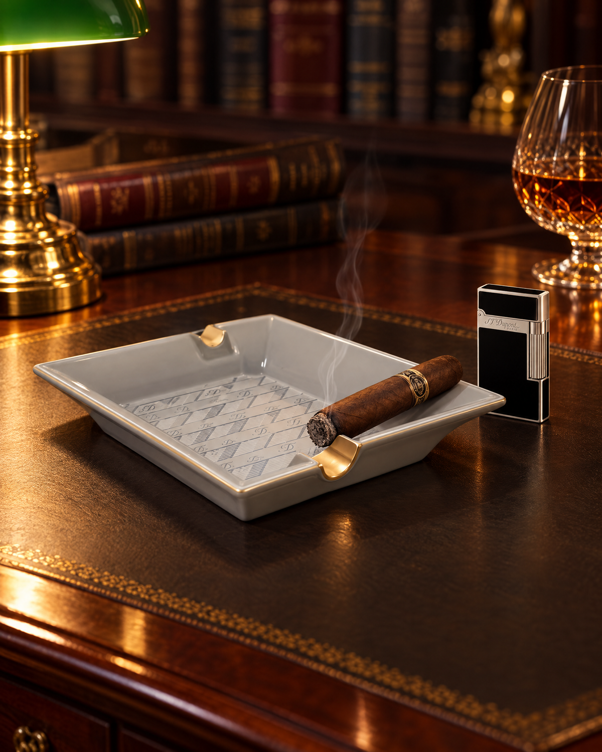 S.T. Dupont Monogram 1872 Ashtray — Porcelain, Grey, close-up on a leather desk blotter with a cigar in one gilt rest and a Ligne 2 lighter beside it, lamp light