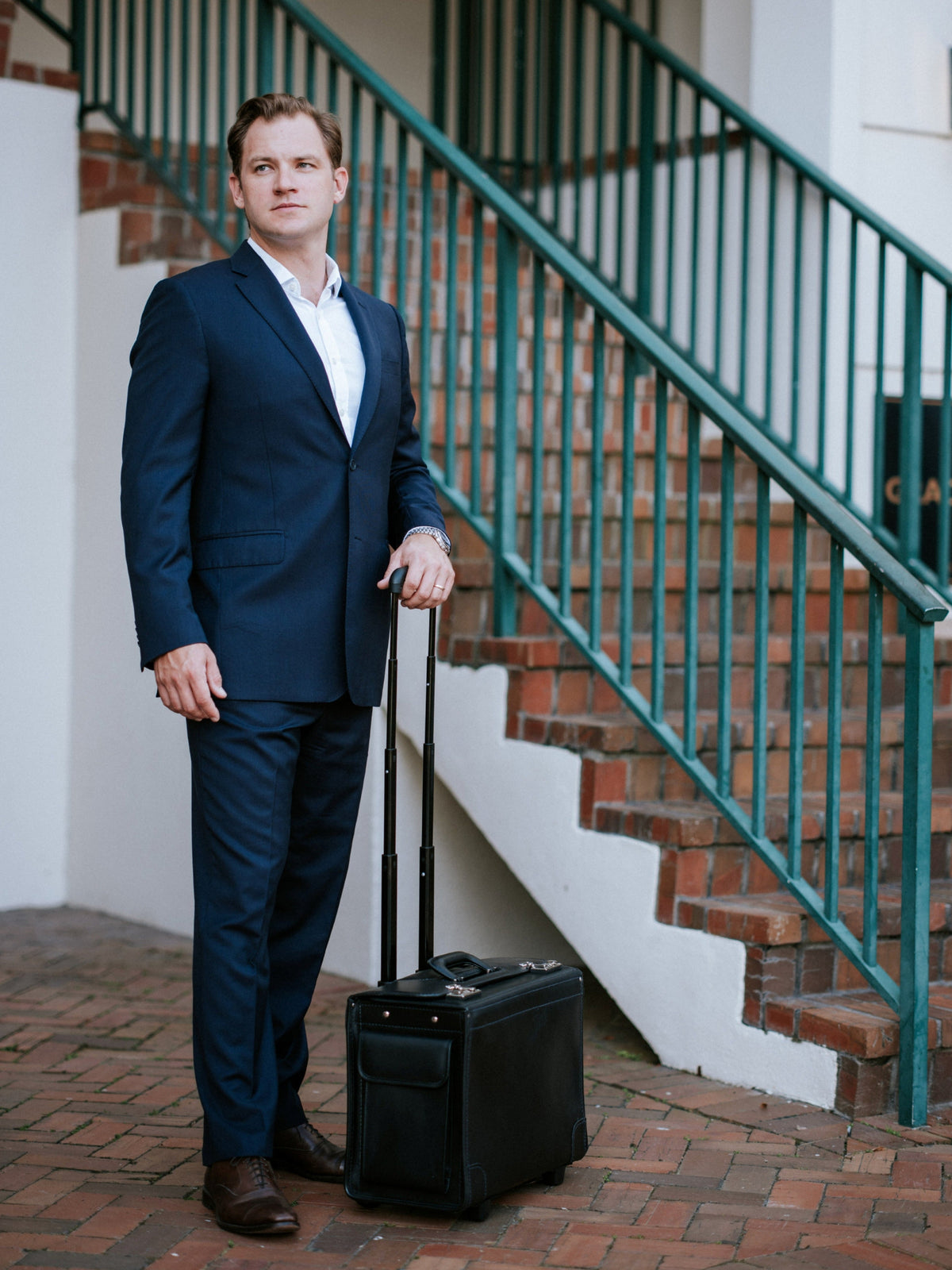 Man in a suit standing with the black Litigator wheeled catalog case on a staircase