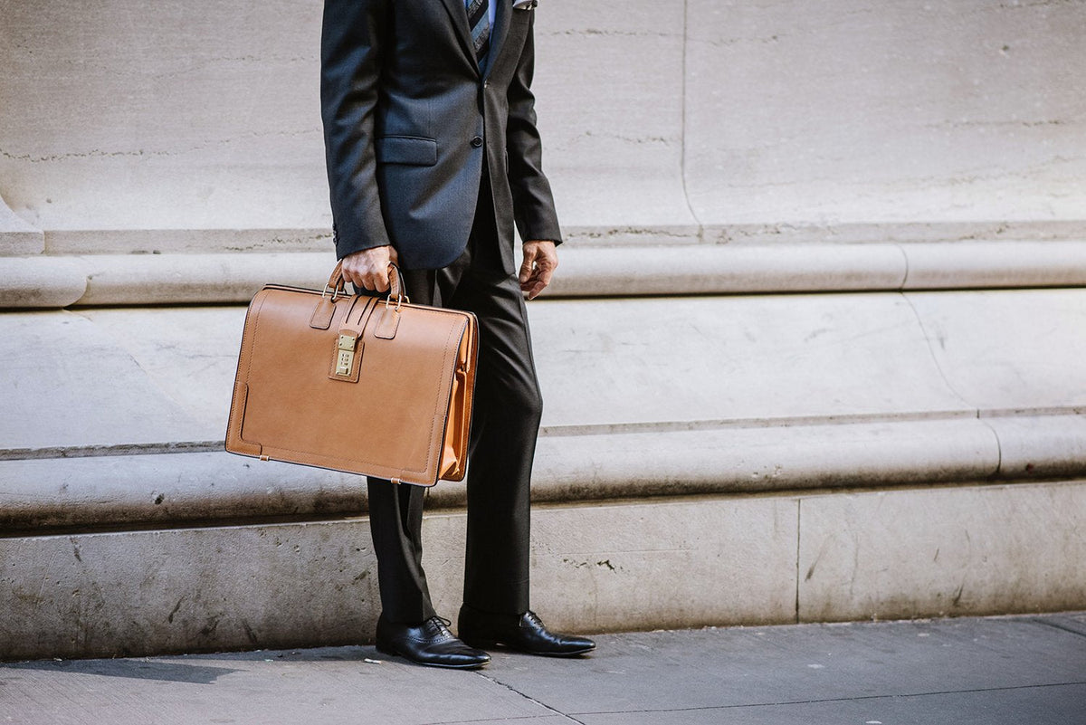 Tan Churchill briefcase carried at the side, close view of the frame-top handle