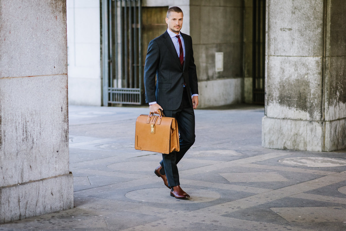 Man in a suit standing with the tan Churchill briefcase, courthouse steps behind him
