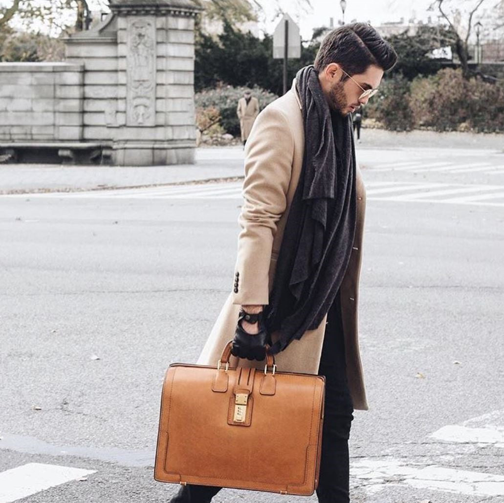 Man in a dark overcoat carrying the tan Churchill Classic Briefcase across a city plaza