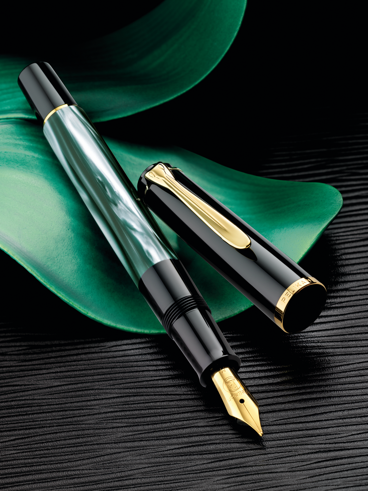 Pelikan M200 fountain pen in green marbled resin with gold trim, uncapped beside its cap on a dark surface