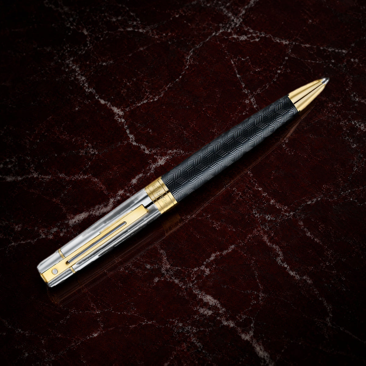 Sheaffer 300 Pen — Engraved Matte Black with Chrome Cap: the ballpoint with an engraved matte black barrel, chrome cap and PVD gold trim, on garnet marble