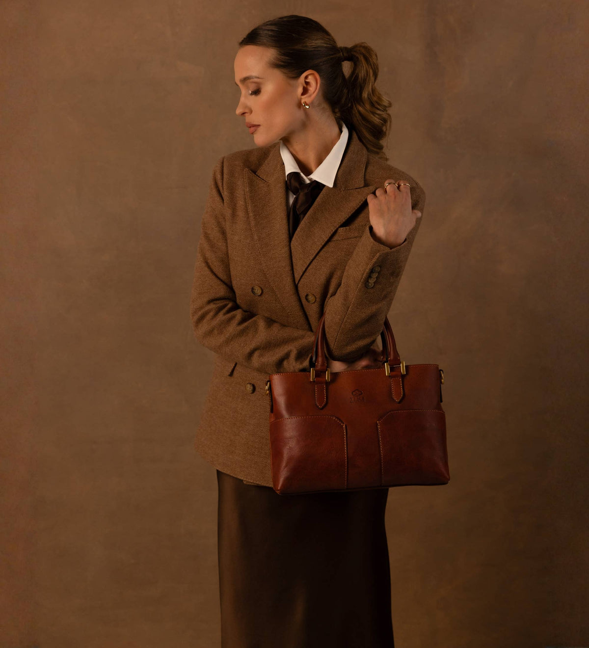 Camilla cognac leather shoulder bag carried by the handles by a model
