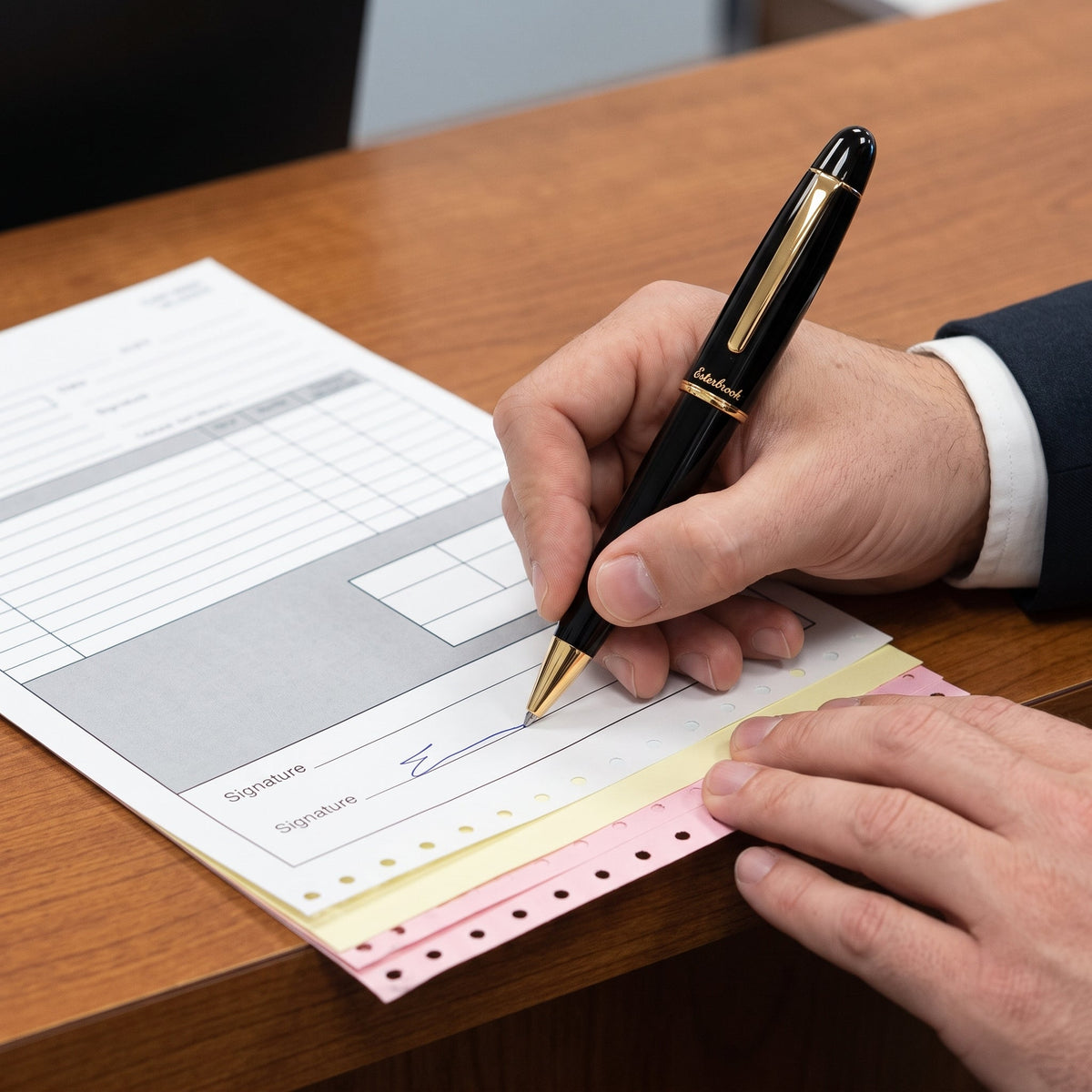 A man in a dark suit signing a multi-part carbonless form with the Esterbrook Estie Ballpoint in Ebony, cap posted on the barrel, the white, yellow and pink layers of the set fanned along the perforated edge