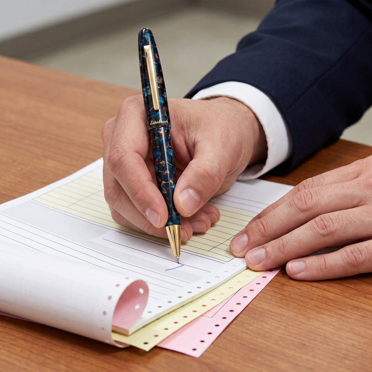 A man in a dark suit signing a multi-part carbonless form with the Esterbrook Estie Ballpoint in Nouveau Bleu, cap posted on the barrel, the white, yellow and pink layers of the set fanned along the perforated edge