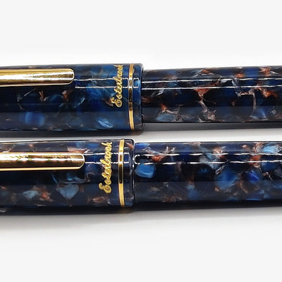 Close view of the Nouveau Bleu acrylic on two Esterbrook Estie pens, showing the navy, turquoise and copper mosaic chips beneath the gloss and the gold Esterbrook script on each cap band