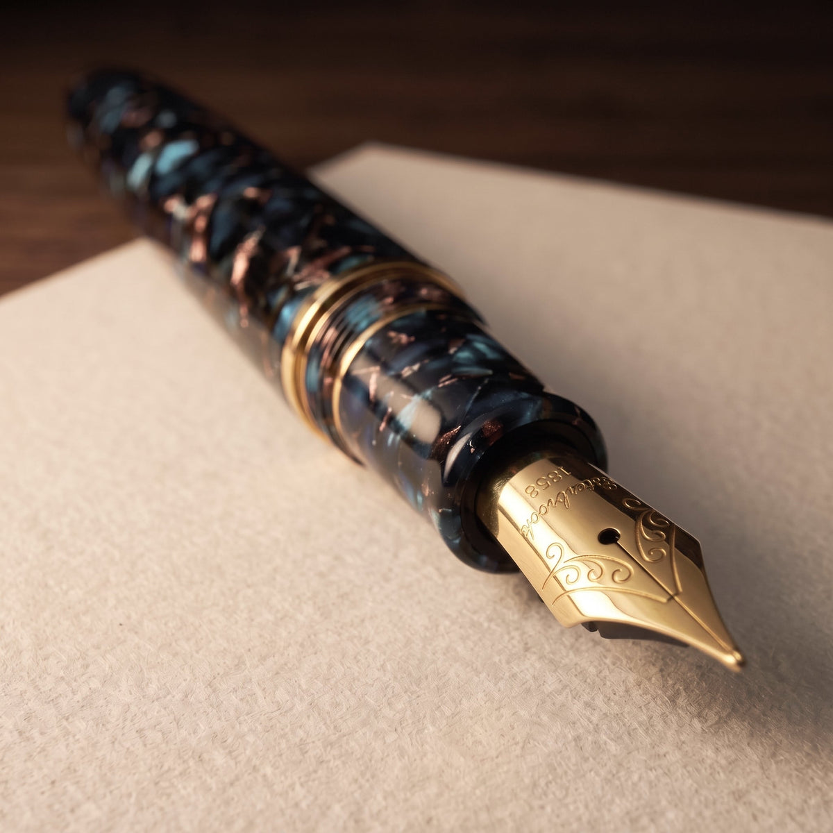 Macro view of the Esterbrook Estie solid 18-carat gold Medium nib, engraved with scrollwork and marked Esterbrook 1858, on the Nouveau Bleu mosaic acrylic section