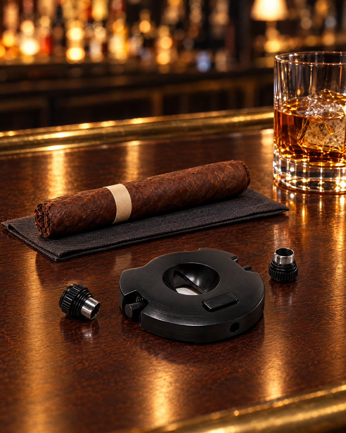 Xceed V-cut and punch cigar cutter in black with its two punch caps, beside an unlit cigar on a hotel bar