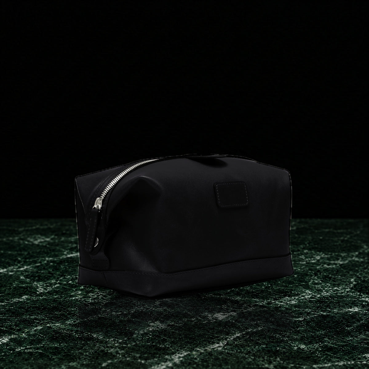Ryder full-grain leather dopp kit in black, three-quarter view on dark green marble