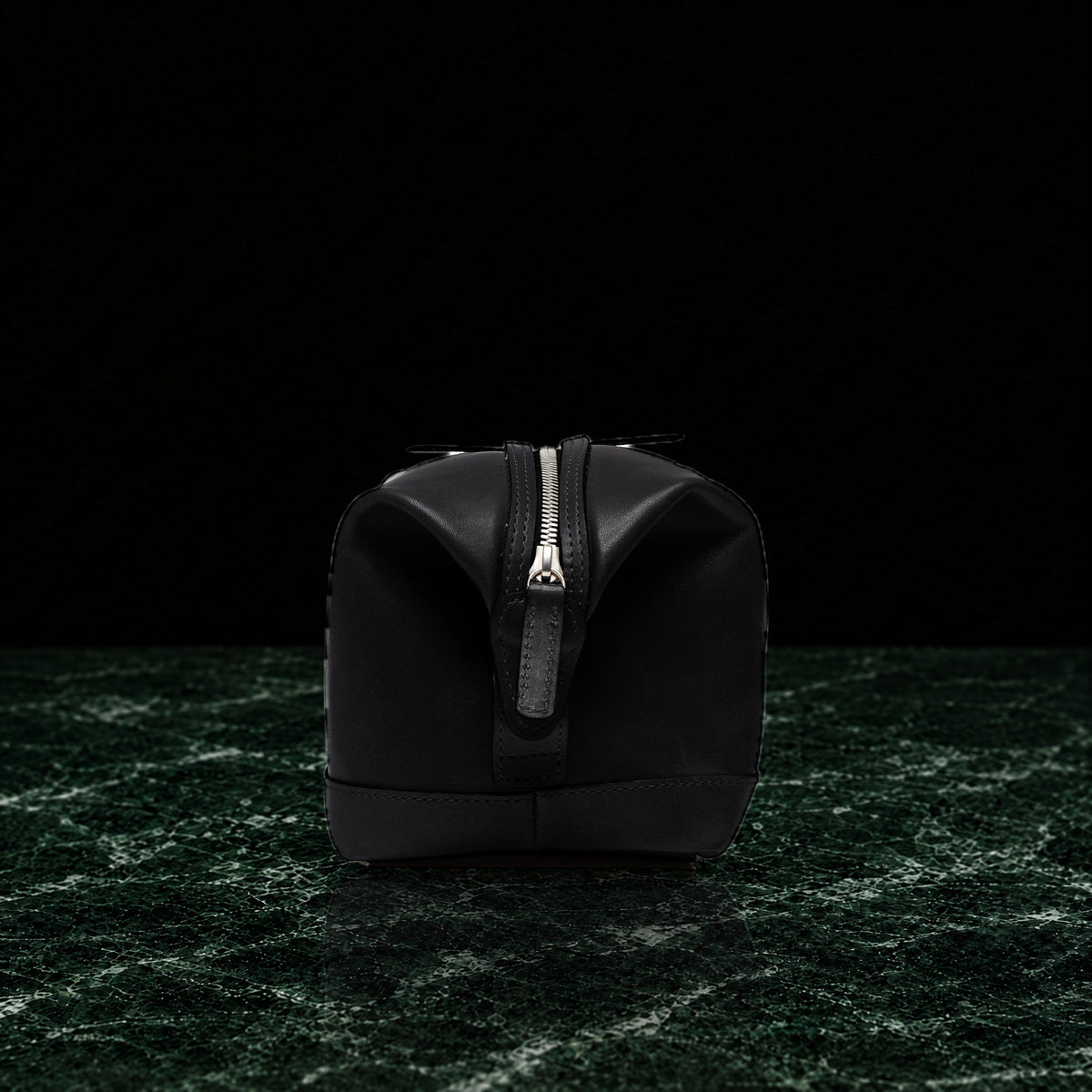 Ryder full-grain leather dopp kit in black, end view showing the top zip on dark green marble