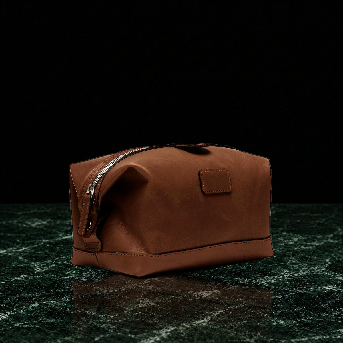 Ryder full-grain leather dopp kit in brown, three-quarter view on dark green marble