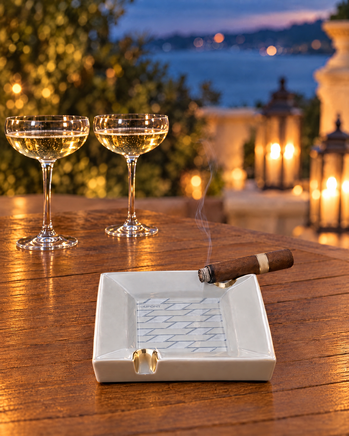 S.T. Dupont Monogram 1872 Ashtray — Porcelain, Grey, a cigar resting in its rim on a terrace table at dusk, two champagne coupes set down behind it