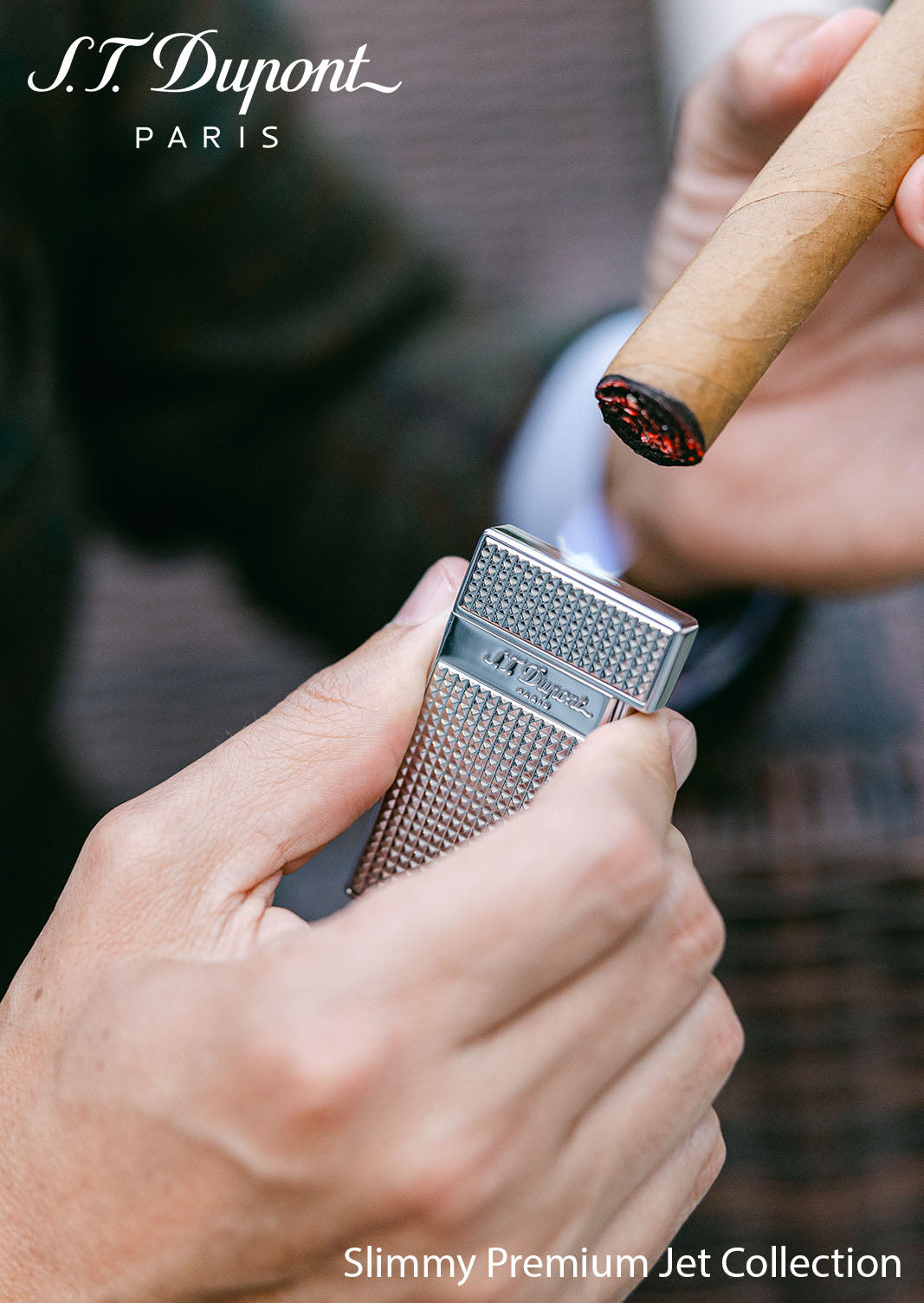 A hand holding the chrome S.T. Dupont Slimmy lighter beside a lit cigar, captioned Slimmy Premium Jet Collection