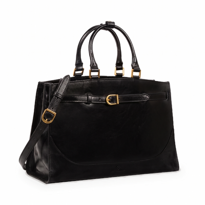 Shirley — Women's Leather Work Tote in black Italian Vachetta, three-quarter view with shoulder strap and brass buckles, on a white background