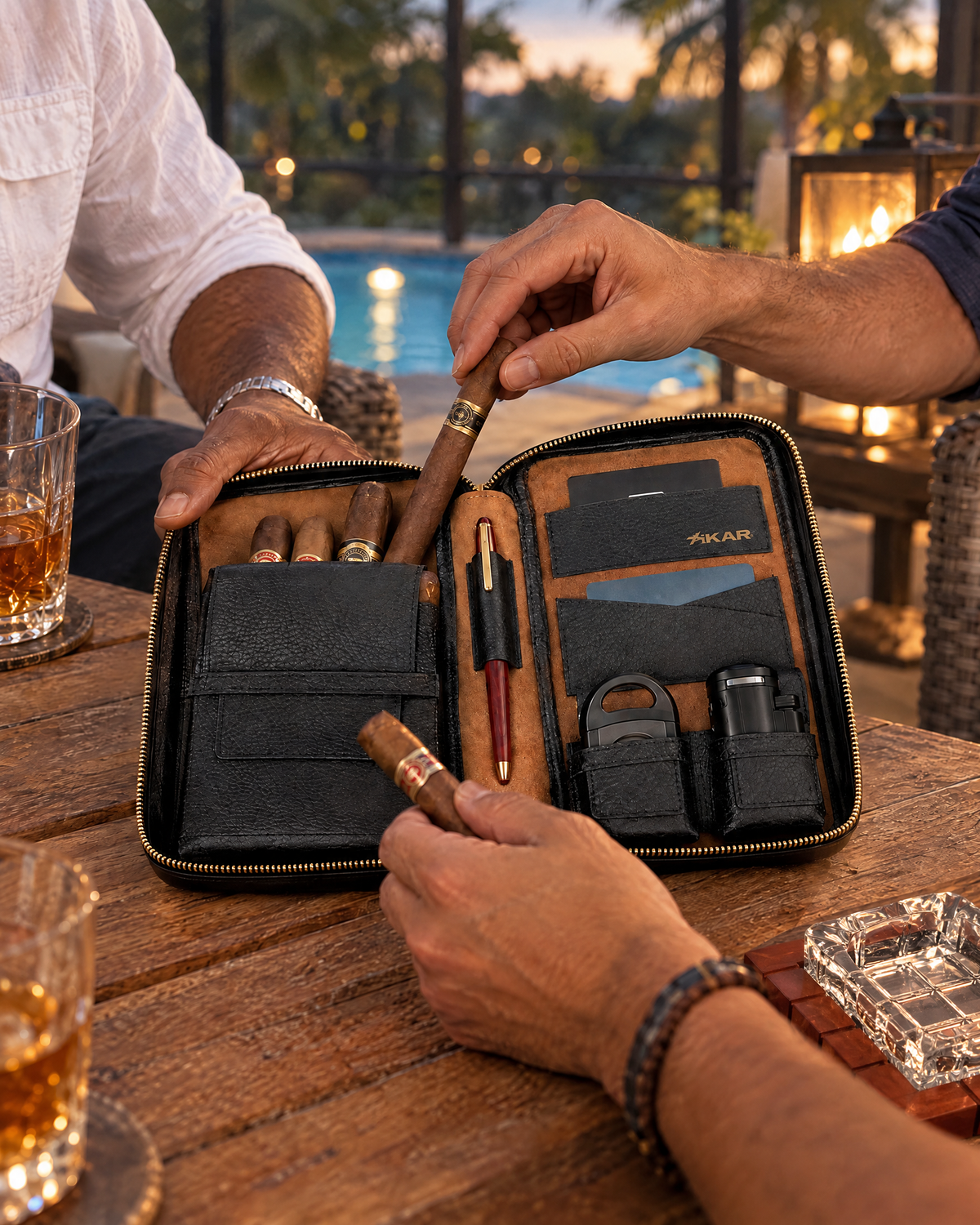 Xikar Sentinel Leather Cigar Case open on a teak table on a Florida lanai at dusk as friends draw unlit cigars from its main pocket, a pen in the leather loop, a cutter and lighter in the side pockets, and a wood and crystal cross-hatched ashtray beside it