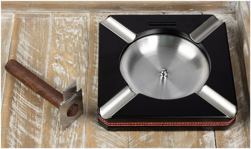 Leather-trim cigar ashtray with cutter on a wood table, cigars beside it