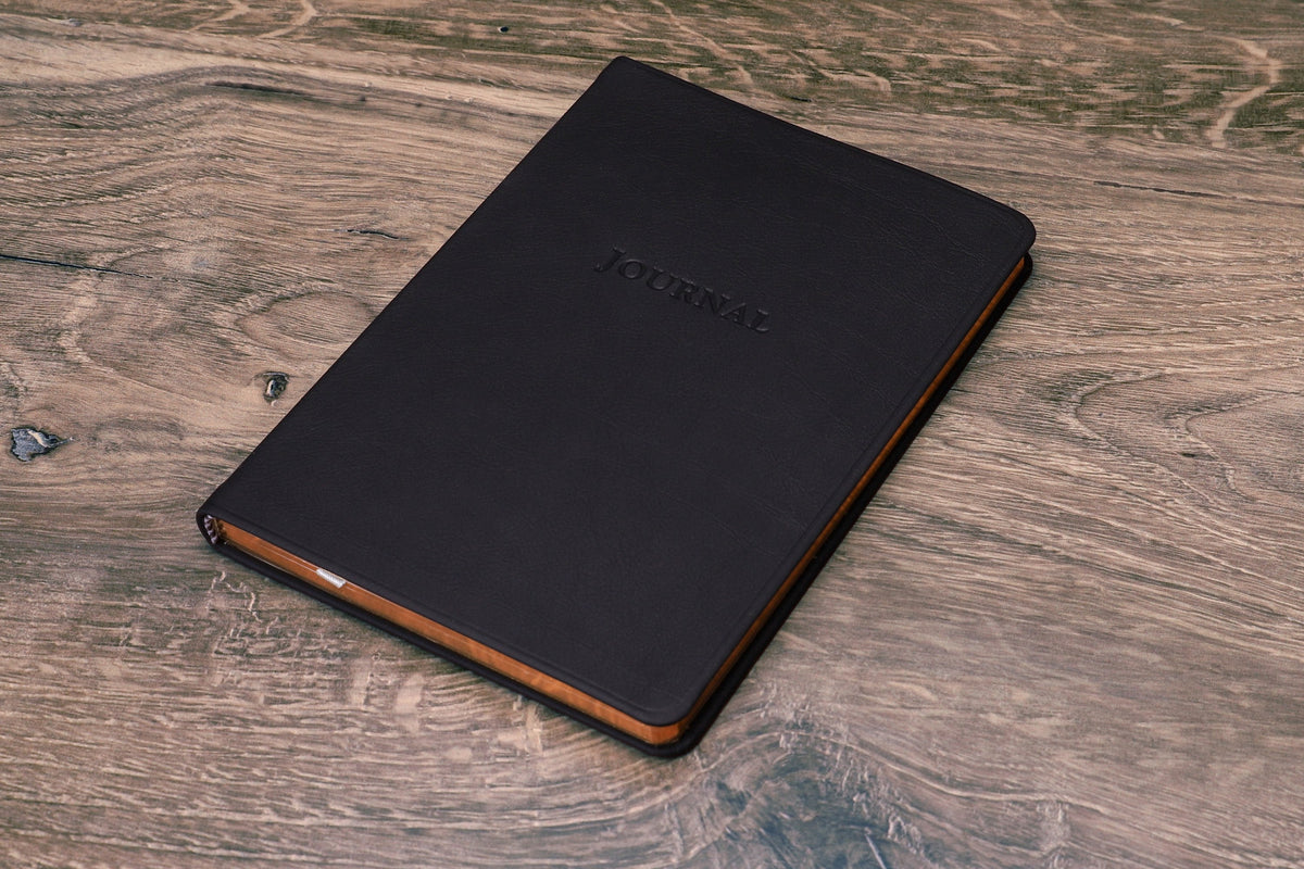 Desk Leather Journal in black leather, closed, cover on a wood desk