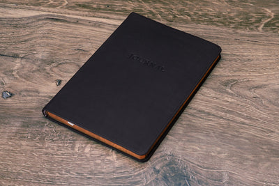 Desk Leather Journal in black leather, closed, cover on a wood desk