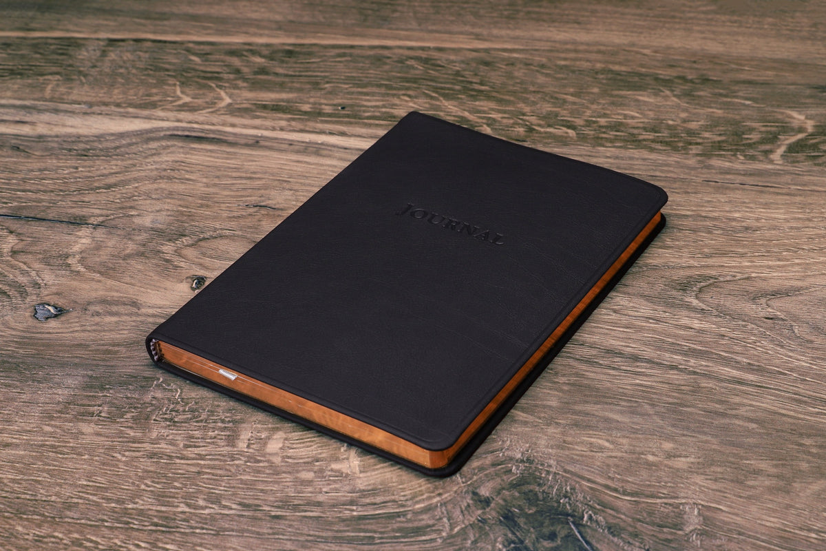Desk Leather Journal in black, closed at an angle showing the spine and gilt page edges