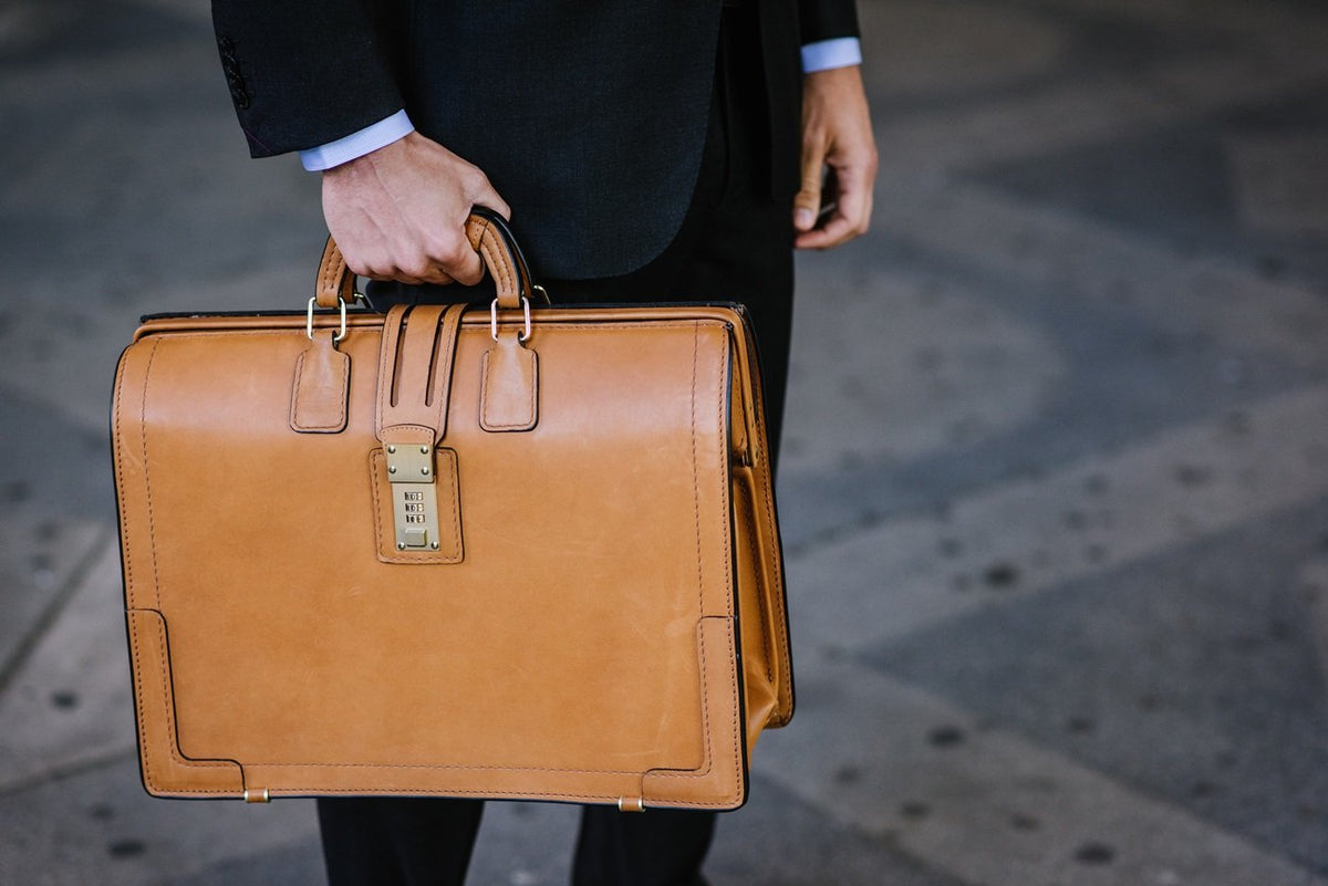 Tan Churchill Classic Briefcase set on a stone ledge, frame top and brass lock visible