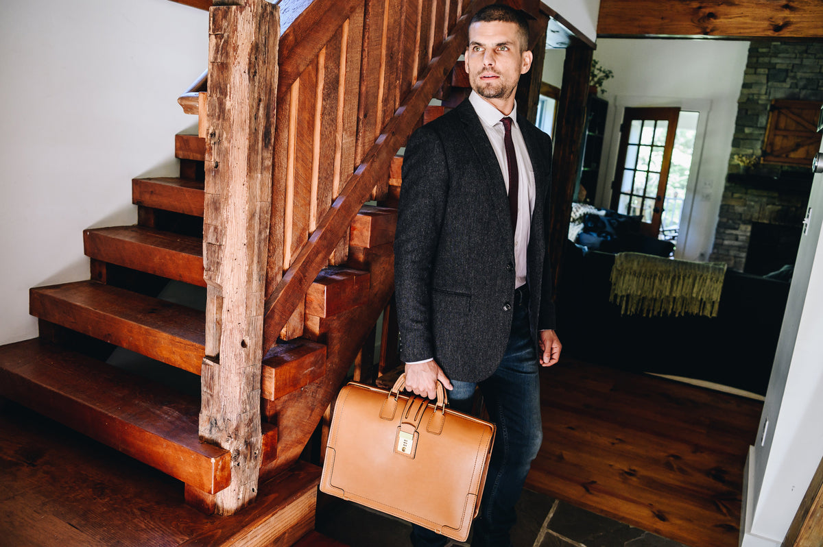 Man in a suit holding the tan Churchill briefcase on a wooden staircase